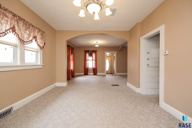 carpeted entryway with baseboards, visible vents, arched walkways, and a notable chandelier