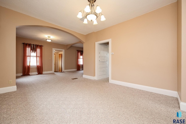 spare room featuring arched walkways, light carpet, a chandelier, and baseboards