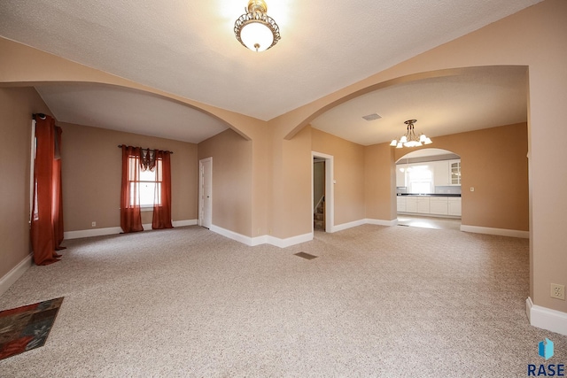 spare room with arched walkways, a notable chandelier, visible vents, baseboards, and carpet