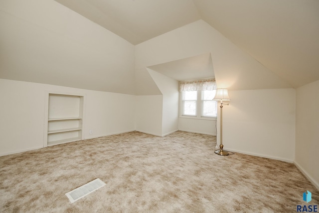 additional living space featuring baseboards, visible vents, lofted ceiling, carpet flooring, and built in shelves