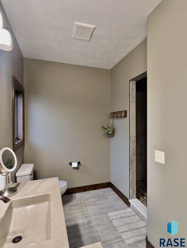 bathroom featuring baseboards, visible vents, toilet, a tile shower, and a sink