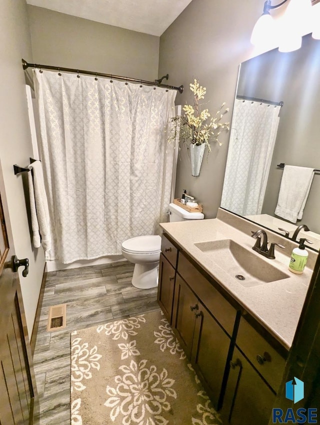 full bath featuring toilet, visible vents, wood finished floors, and vanity