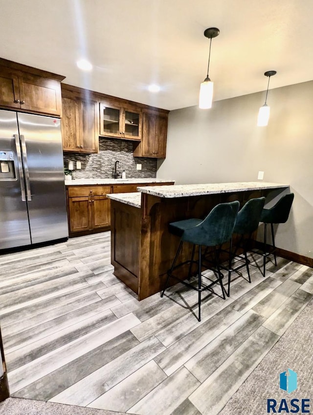 bar with decorative light fixtures, stainless steel fridge, backsplash, and light wood finished floors