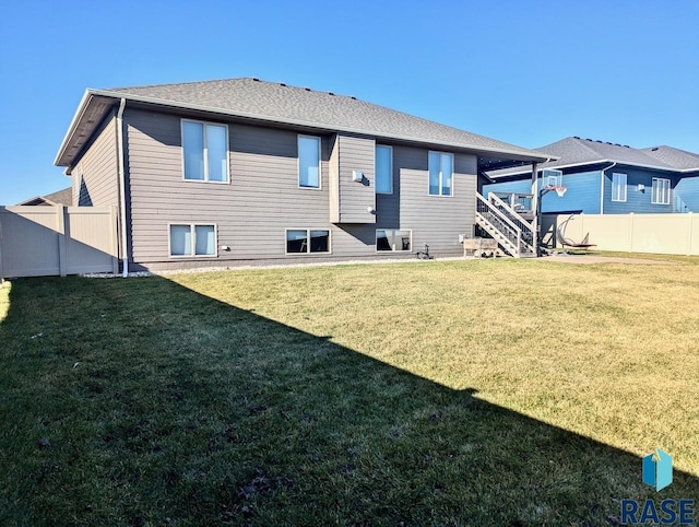 rear view of property with a fenced backyard, stairway, a lawn, and roof with shingles