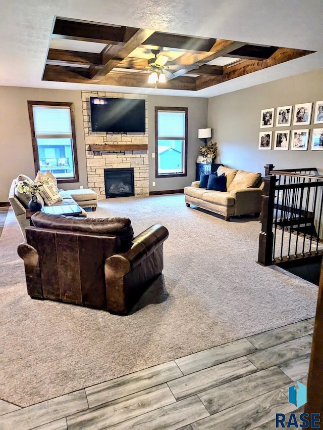 living area featuring a wealth of natural light, coffered ceiling, beamed ceiling, and a stone fireplace