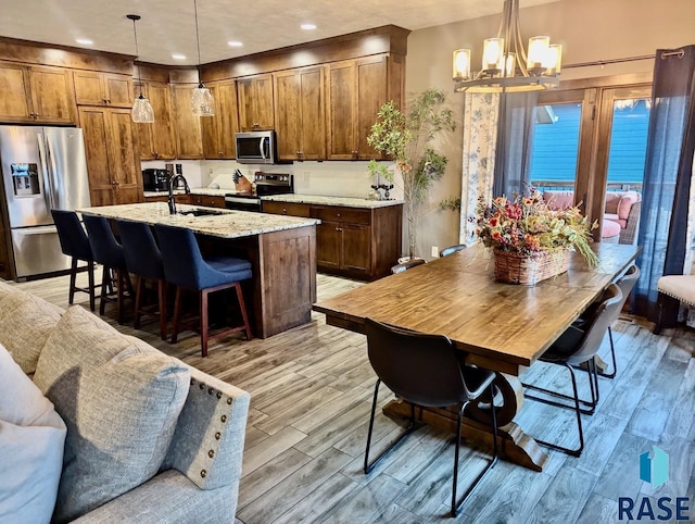 kitchen featuring appliances with stainless steel finishes, a chandelier, a sink, and light wood finished floors