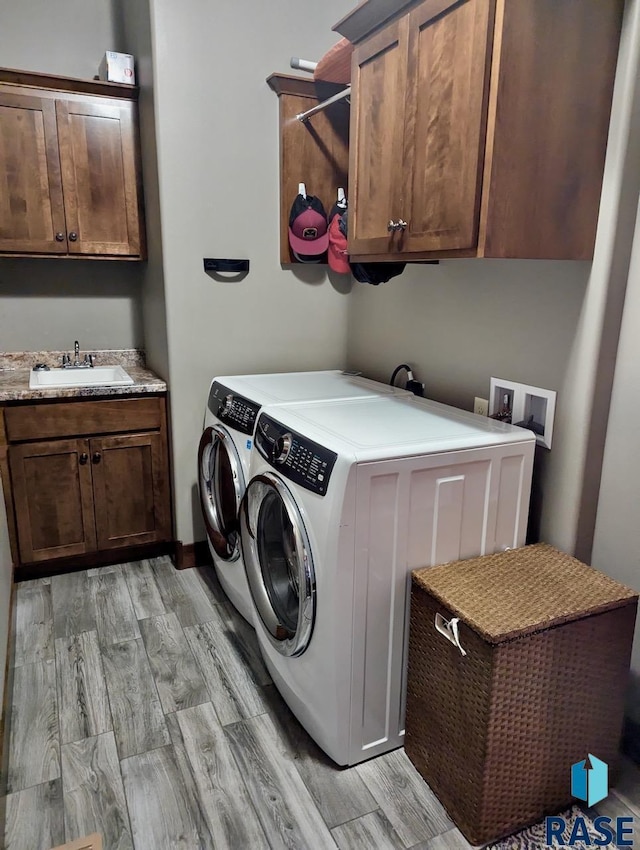 washroom featuring light wood-style floors, washing machine and dryer, cabinet space, and a sink