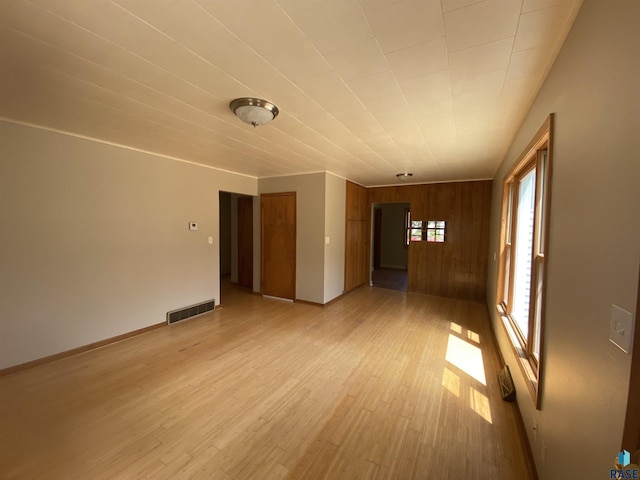 empty room with light wood finished floors, baseboards, wooden walls, and visible vents