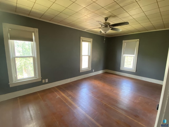 empty room with a ceiling fan, crown molding, baseboards, and wood finished floors