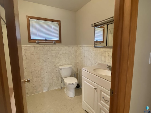 half bathroom with tile walls, wainscoting, vanity, and toilet