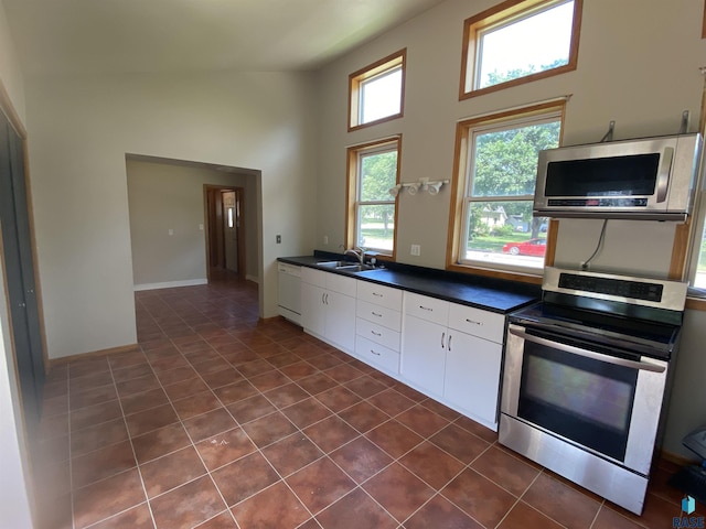 kitchen featuring dark countertops, appliances with stainless steel finishes, white cabinetry, a sink, and dark tile patterned flooring