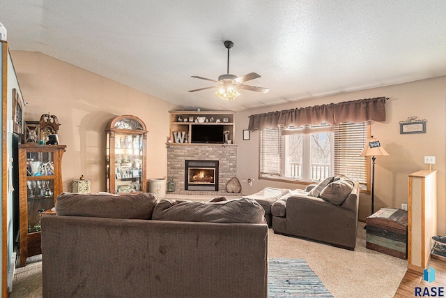 living room featuring lofted ceiling, ceiling fan, a textured ceiling, a fireplace, and light wood-type flooring