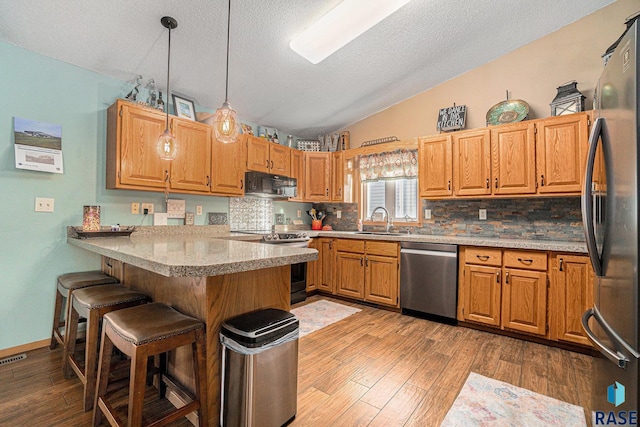 kitchen featuring stainless steel appliances, vaulted ceiling, a sink, a peninsula, and a kitchen bar