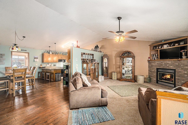 living room featuring dark wood-style floors, ceiling fan, vaulted ceiling, and a brick fireplace