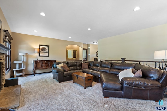 carpeted living area featuring recessed lighting, arched walkways, baseboards, and a stone fireplace