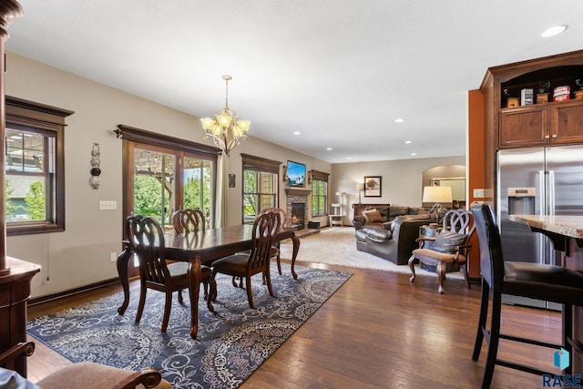 dining space with a warm lit fireplace, recessed lighting, wood finished floors, and a notable chandelier