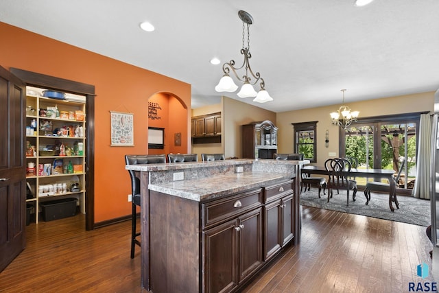 kitchen with dark brown cabinetry, a breakfast bar, dark wood-style flooring, and decorative light fixtures