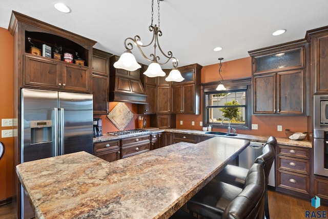 kitchen featuring custom range hood, a kitchen island, light stone counters, stainless steel appliances, and a sink