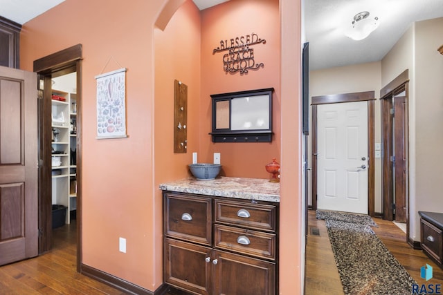 corridor featuring dark wood-type flooring, arched walkways, and baseboards