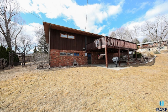 back of house with a yard, brick siding, a patio, and a wooden deck