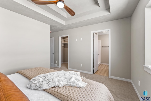 bedroom featuring light carpet, baseboards, a tray ceiling, a walk in closet, and a closet