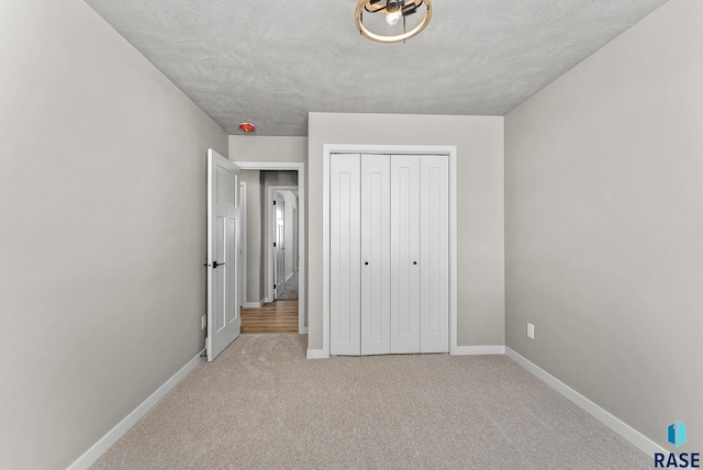 unfurnished bedroom featuring a closet, carpet flooring, a textured ceiling, and baseboards