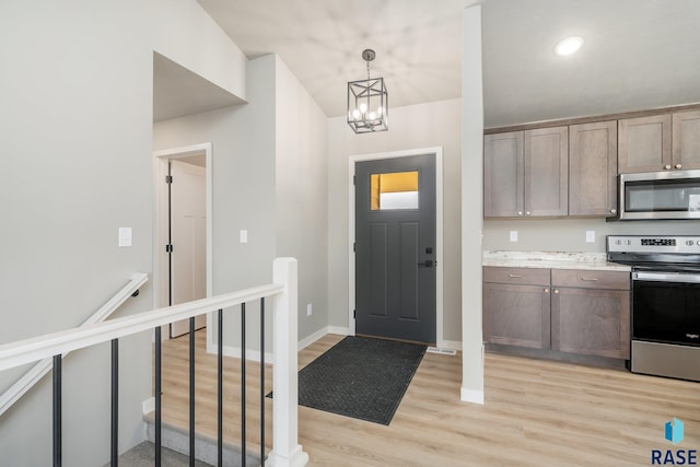 foyer featuring light wood-type flooring, an inviting chandelier, and baseboards