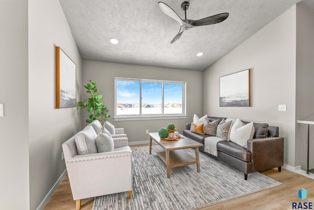 living area featuring baseboards, lofted ceiling, ceiling fan, a textured ceiling, and light wood-type flooring