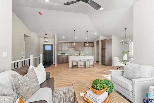 living area featuring lofted ceiling, light wood-style flooring, recessed lighting, and ceiling fan with notable chandelier