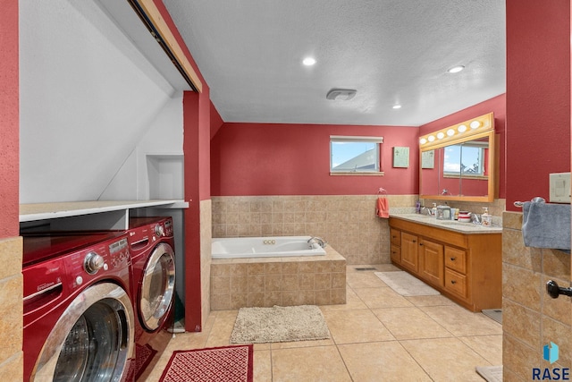 full bath featuring a garden tub, washing machine and dryer, vanity, a textured ceiling, and tile patterned floors