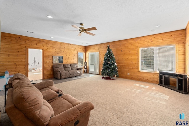 carpeted living area featuring a textured ceiling, wooden walls, recessed lighting, visible vents, and a ceiling fan