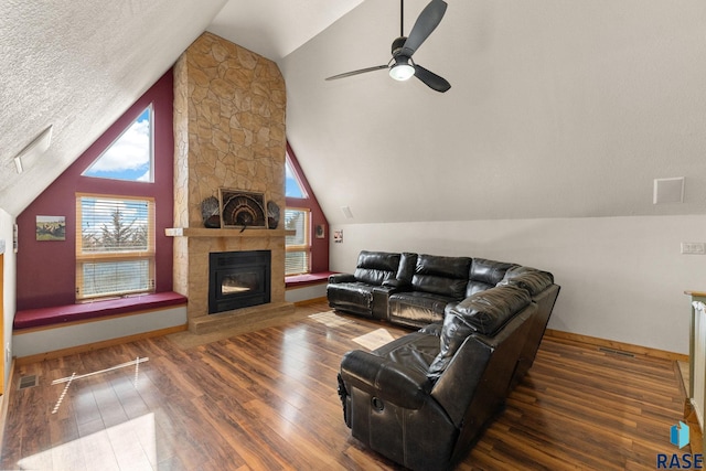 living area featuring visible vents, wood finished floors, vaulted ceiling, a textured ceiling, and a stone fireplace