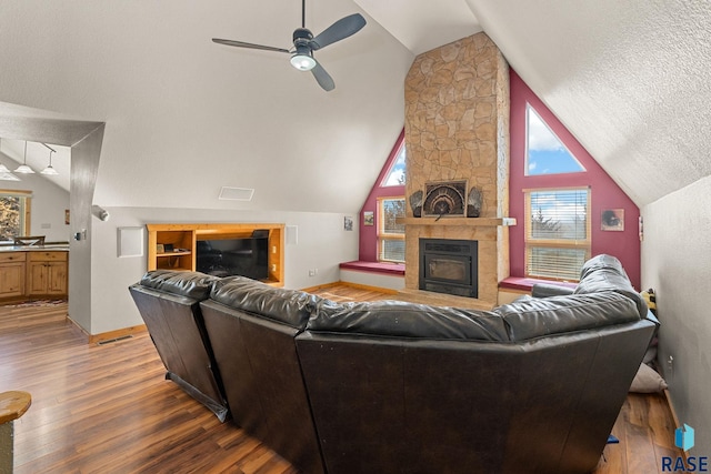 living room with vaulted ceiling, a stone fireplace, baseboards, and wood finished floors