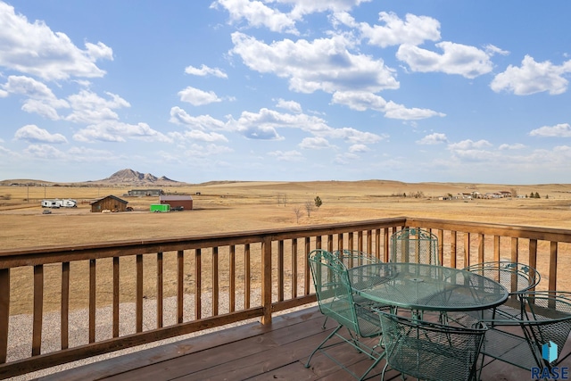 wooden terrace featuring a rural view, a mountain view, and outdoor dining space