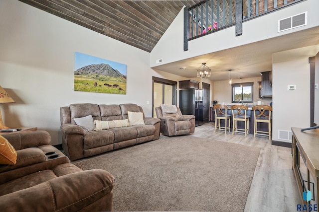 living room featuring light wood finished floors, a notable chandelier, visible vents, and high vaulted ceiling