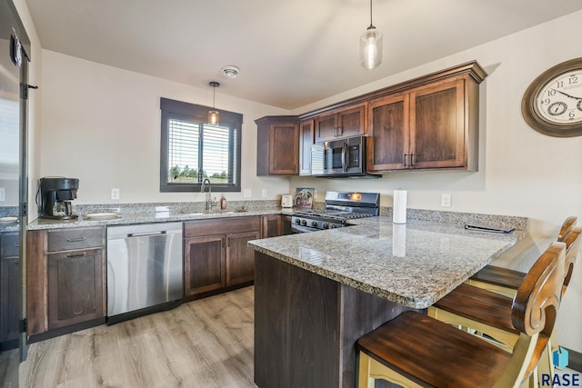 kitchen featuring light stone counters, a peninsula, hanging light fixtures, stainless steel appliances, and a sink