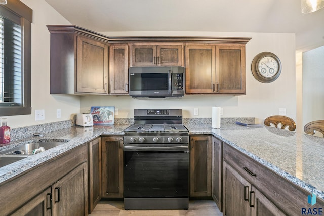 kitchen with a sink, a peninsula, appliances with stainless steel finishes, and light stone counters