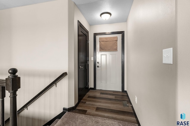 hall featuring a textured ceiling, baseboards, dark wood-style flooring, and an upstairs landing