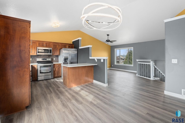 kitchen with appliances with stainless steel finishes, open floor plan, vaulted ceiling, light countertops, and backsplash