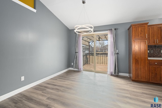 unfurnished dining area featuring light wood-type flooring, baseboards, vaulted ceiling, and a notable chandelier