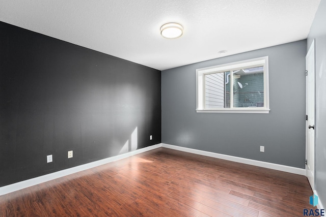 unfurnished room featuring a textured ceiling, wood finished floors, and baseboards