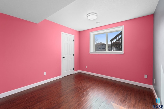 empty room with baseboards and dark wood-type flooring