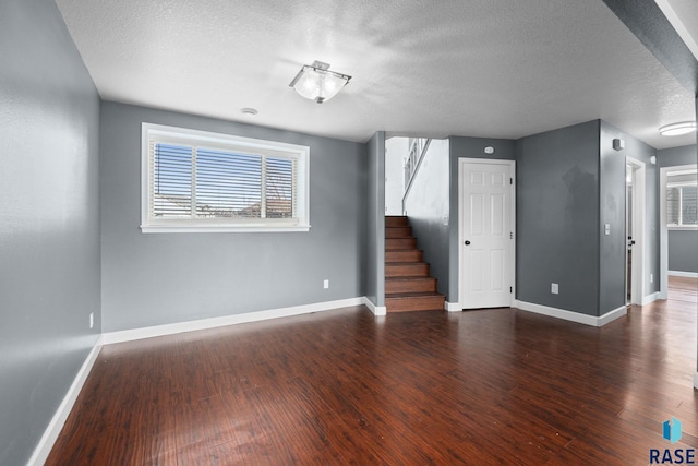 empty room with stairs, a textured ceiling, wood finished floors, and baseboards