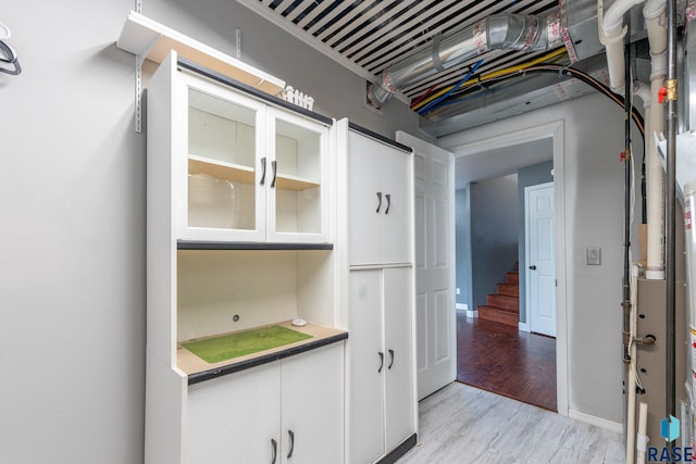 kitchen with light wood-type flooring, baseboards, white cabinetry, and glass insert cabinets