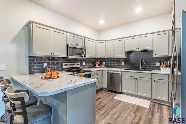 kitchen featuring light wood-style flooring, a peninsula, a sink, appliances with stainless steel finishes, and backsplash