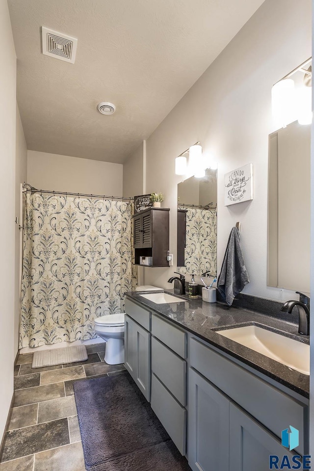 bathroom featuring visible vents, a sink, toilet, and double vanity