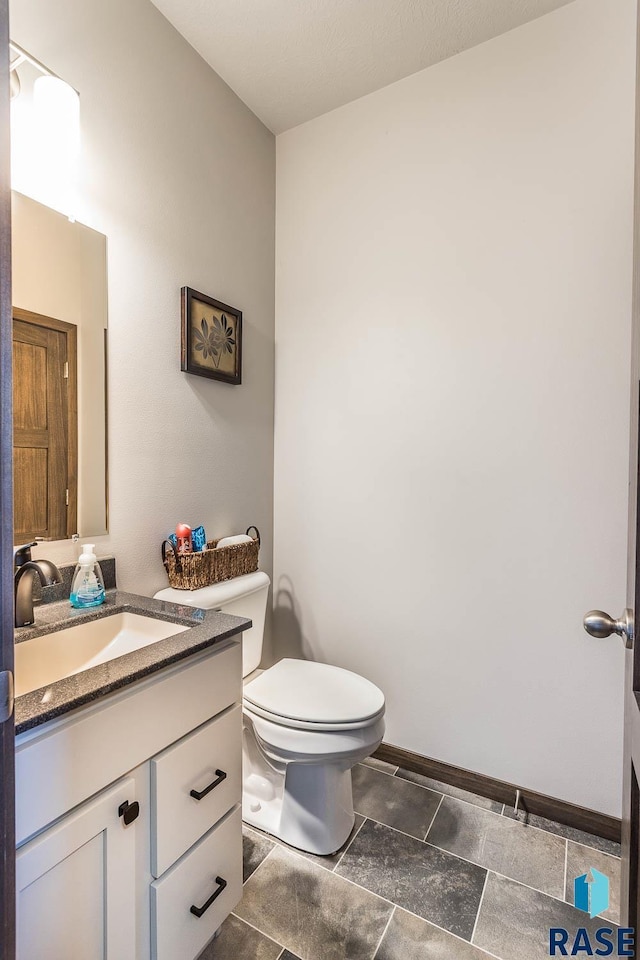 half bath with baseboards, vanity, and toilet