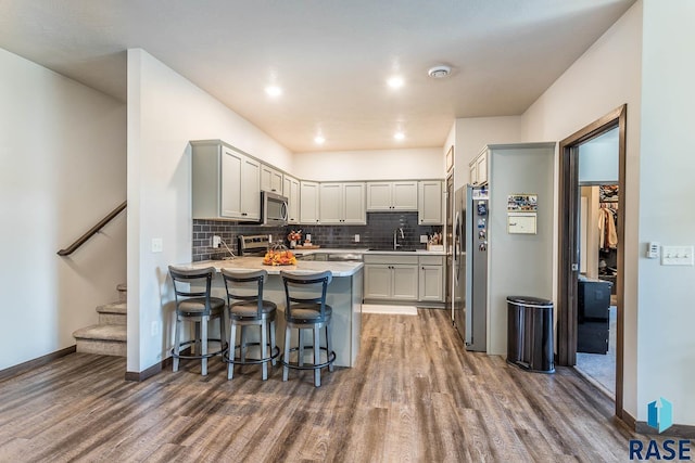 kitchen featuring appliances with stainless steel finishes, wood finished floors, a peninsula, a sink, and backsplash