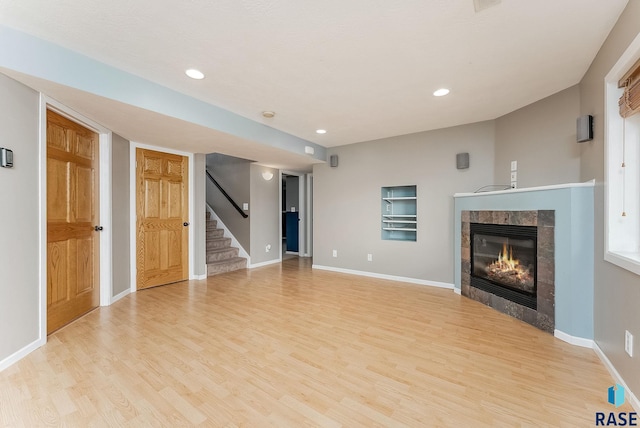 unfurnished living room featuring light wood finished floors, baseboards, stairway, and a tiled fireplace