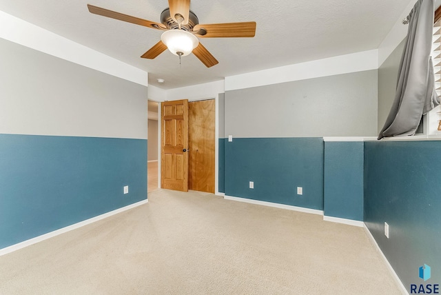 unfurnished room with a textured ceiling, carpet floors, a ceiling fan, and baseboards